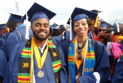 Two students wearing graduation garb at an event