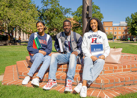 Students wearing Howard sweatshirts, seated on The Yard and smiling