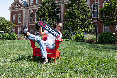 Seated student smiling and holding the Howard GO BISON sign
